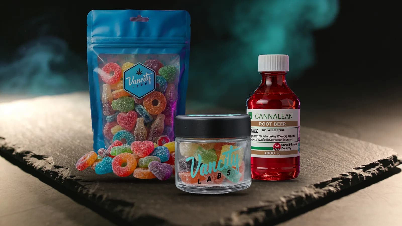 1000mg edible packs: a 1500mg bag of Dripped gummies, a 750mg jar of Handcrafted squares and a 1000mg bottle of Nano CannaLean on dark slate